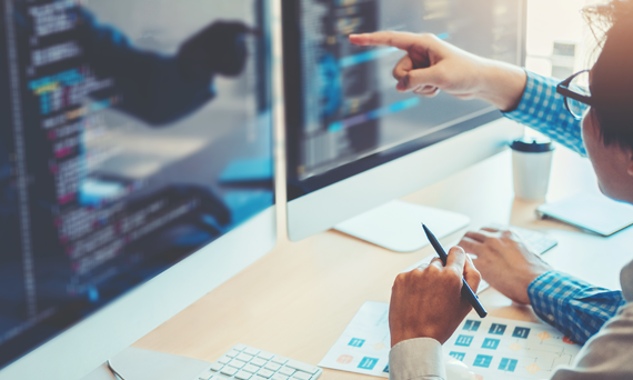 man sitting at desk pointing to monitor