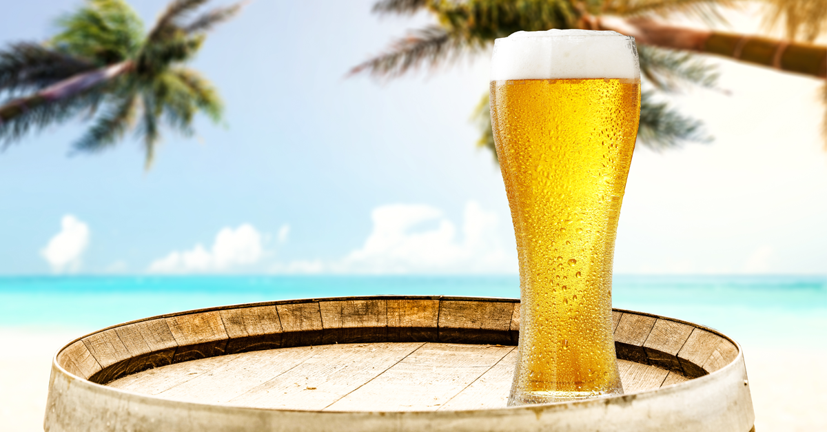 Glass of beer on a table on the beach with palm trees
