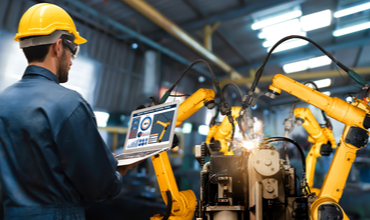 Assembly worker using laptop to control robotic arm assembly line