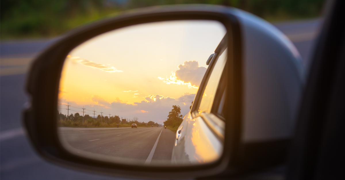car sideview mirror reflecting road and sky